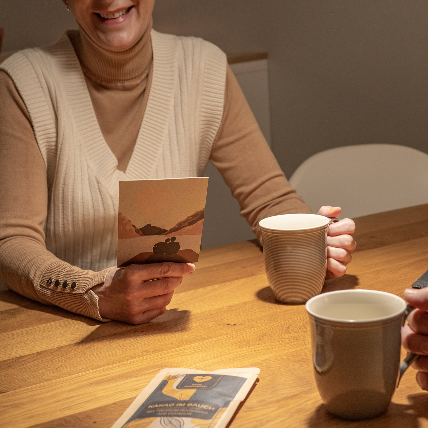 Frau die am Tisch sitzt, einen Tee trinkt und eine Karte vorliest. Vor Ihr liegt ein Kakao.